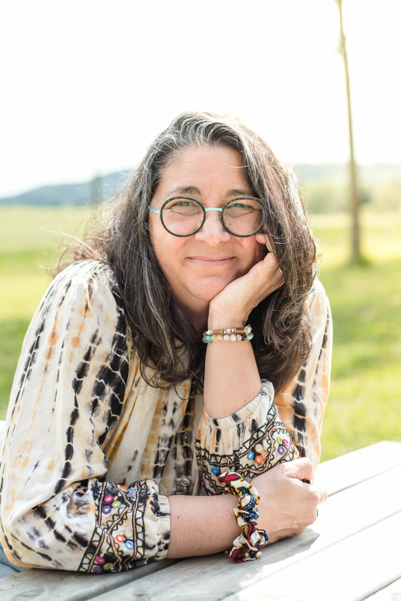 nathalie-makars assise dehors à Toulouse, lunettes rondes turquoise, sourire doux dans une ambiance paisible
